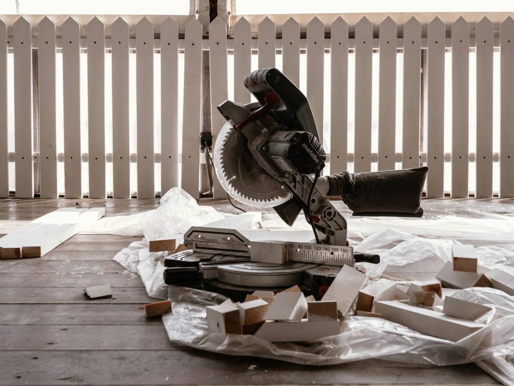 pexels photo 7667619 7667619 A circular saw on a wooden terrace with cut wood pieces and a white fence.