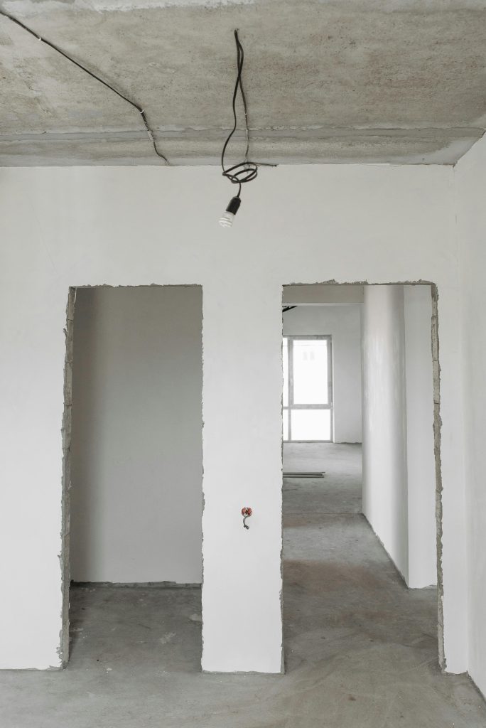 pexels photo 7937304 7937304 Unfinished room interior with white plastered walls and exposed ceiling in a construction site.